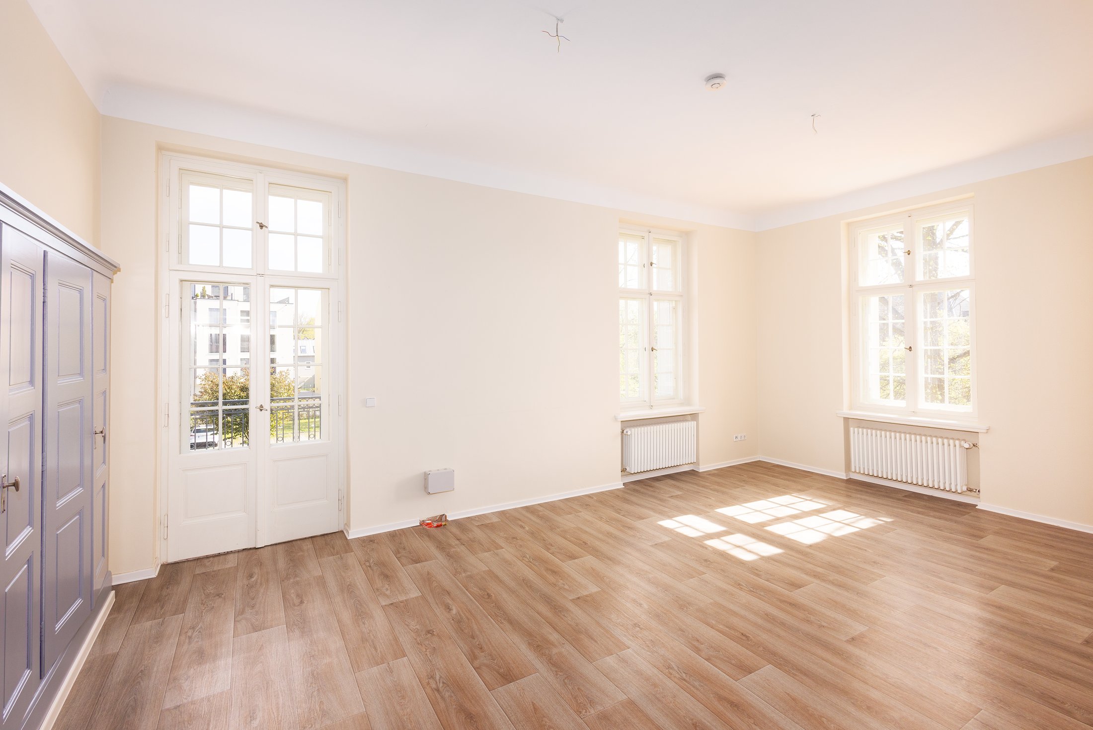 Helles Zimmer mit grauem Einbauschrank, Balkontür und Parkettboden, Projekt Schütze Immobilien