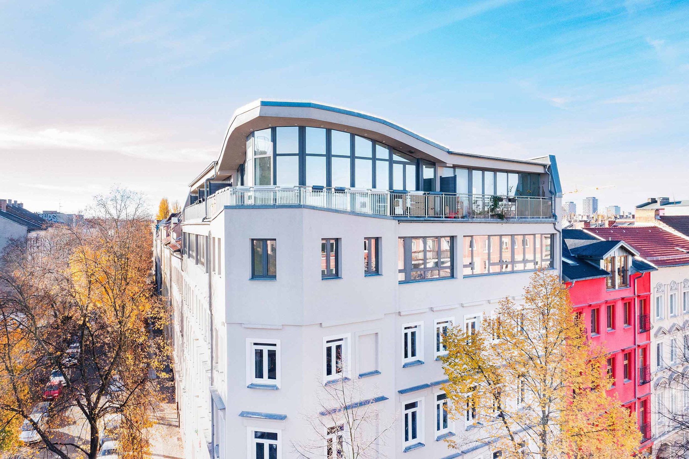 Drohnenaufnahme: Eckgebäude mit geschwungenem Dachgeschoss, Glasfront und umlaufender Terrasse, Projekt Leible & Cie.