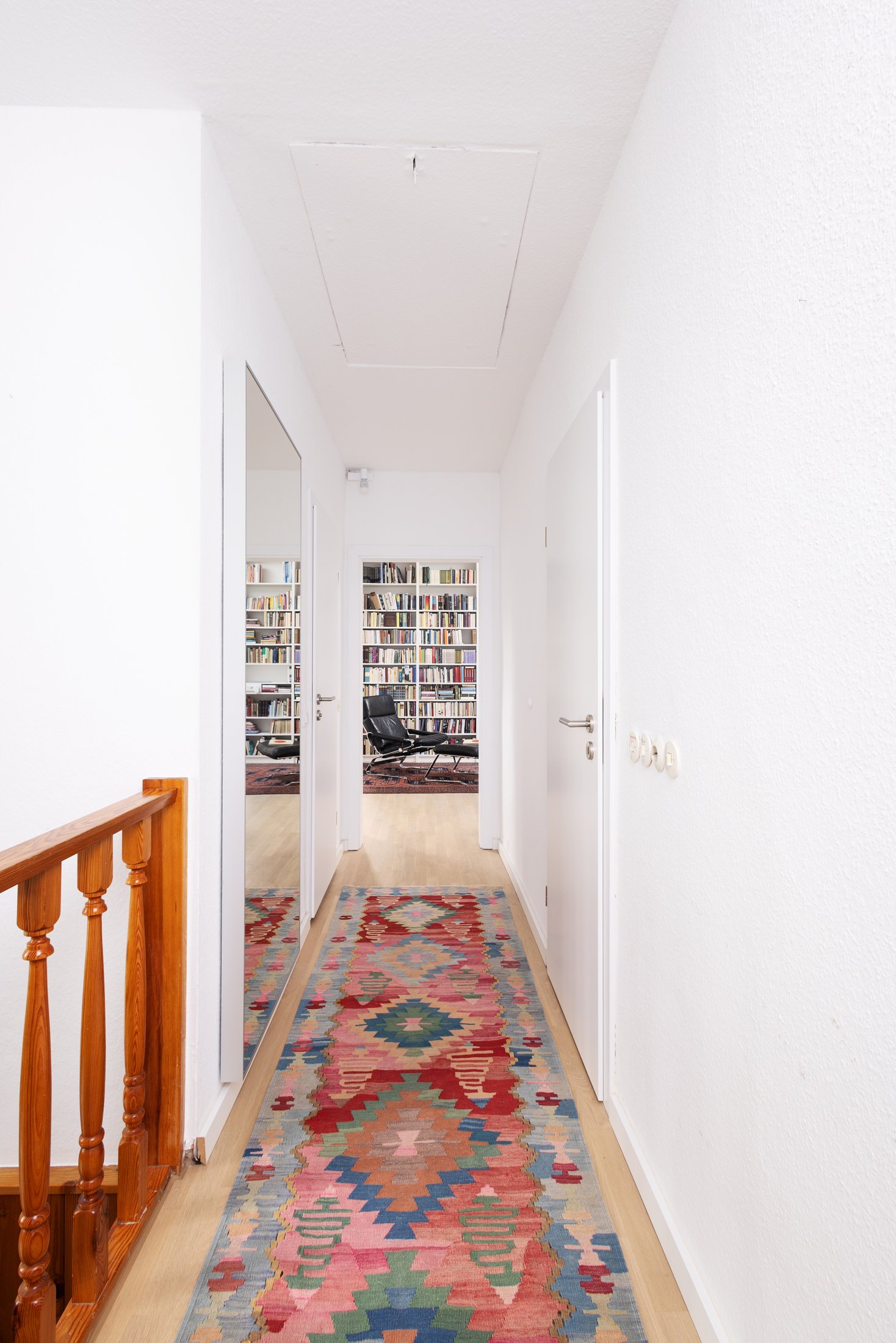 Projekt Taubenweg: Flur mit buntem Kelim-Läufer und Blick in die Bibliothek