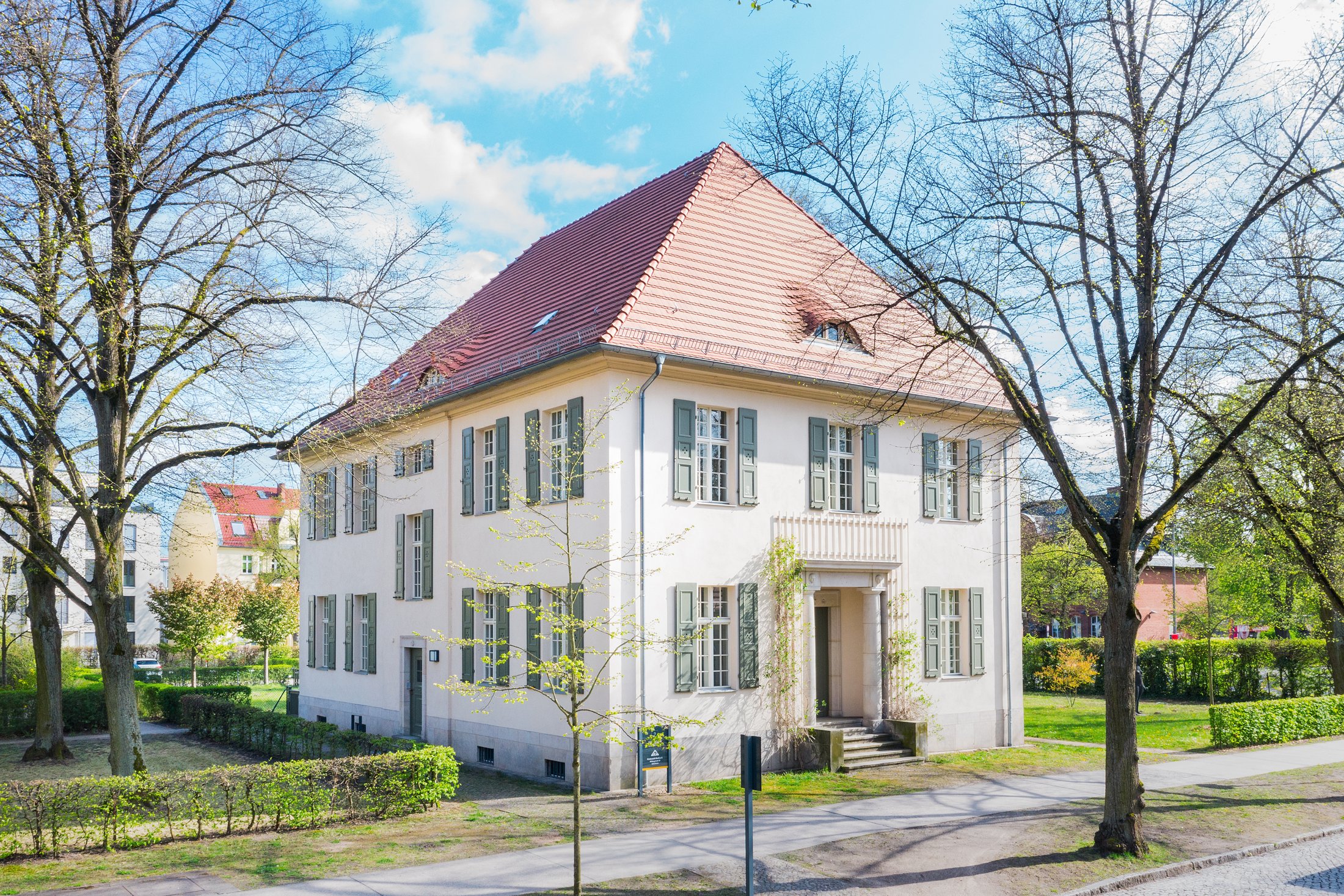 Villa mit rotem Ziegeldach, Säuleneingang und grünen Fensterläden von der Straßenseite, Projekt Schütze Immobilien